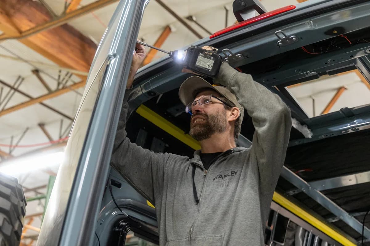 A builder driving fasteners overhead inside a van shell