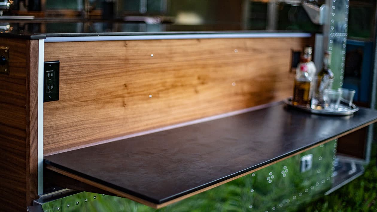 Fold-down black countertop with integrated outlets and wood paneling above aluminum exterior wall, 1953 Silver Streak Clipper