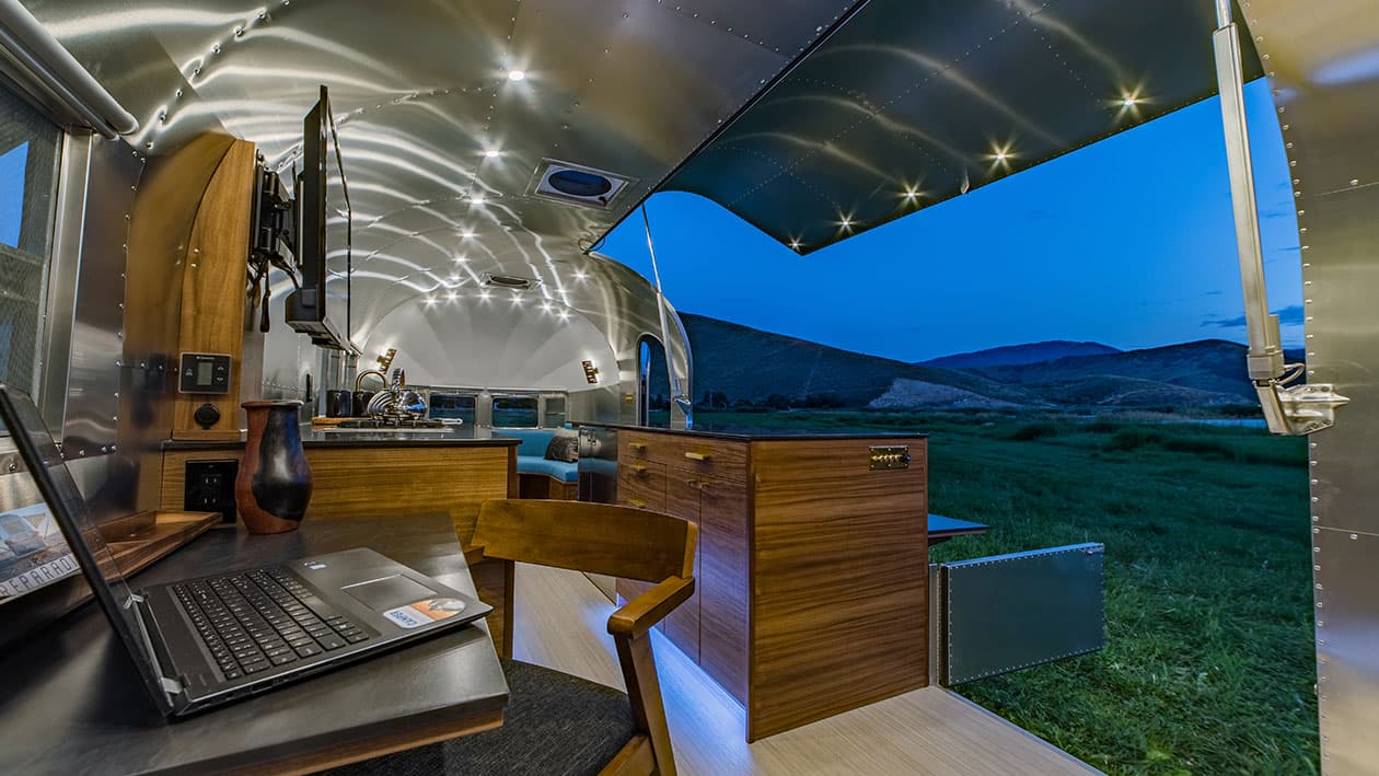 Interior workspace with laptop, walnut cabinetry, LED ceiling lights, and fold-out hatch door open to landscape, 1953 Silver Streak Clipper