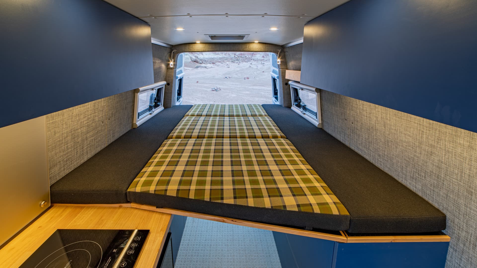 Folded plaid cushions forming full-width bed platform with rear door open and side storage panels, 2021 Sprinter 4x4 VS30