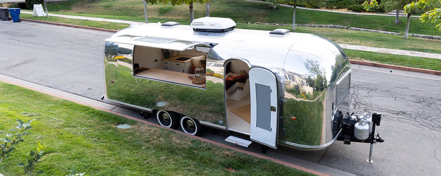 Polished aluminum exterior with rooftop AC, propane tanks, open service window, and entry door open on 1959 Airstream Tradewind