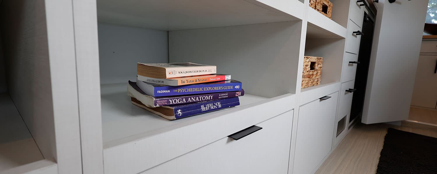 Open shelving with stacked yoga and wellness books next to woven baskets and black drawer handles, 1959 Airstream Tradewind