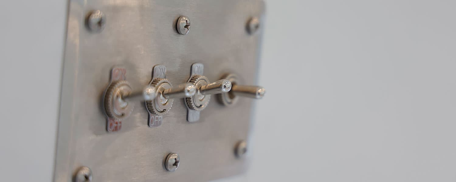 Close-up of three vintage-style metal toggle switches mounted on a brushed metal switch plate, 1959 Airstream Tradewind