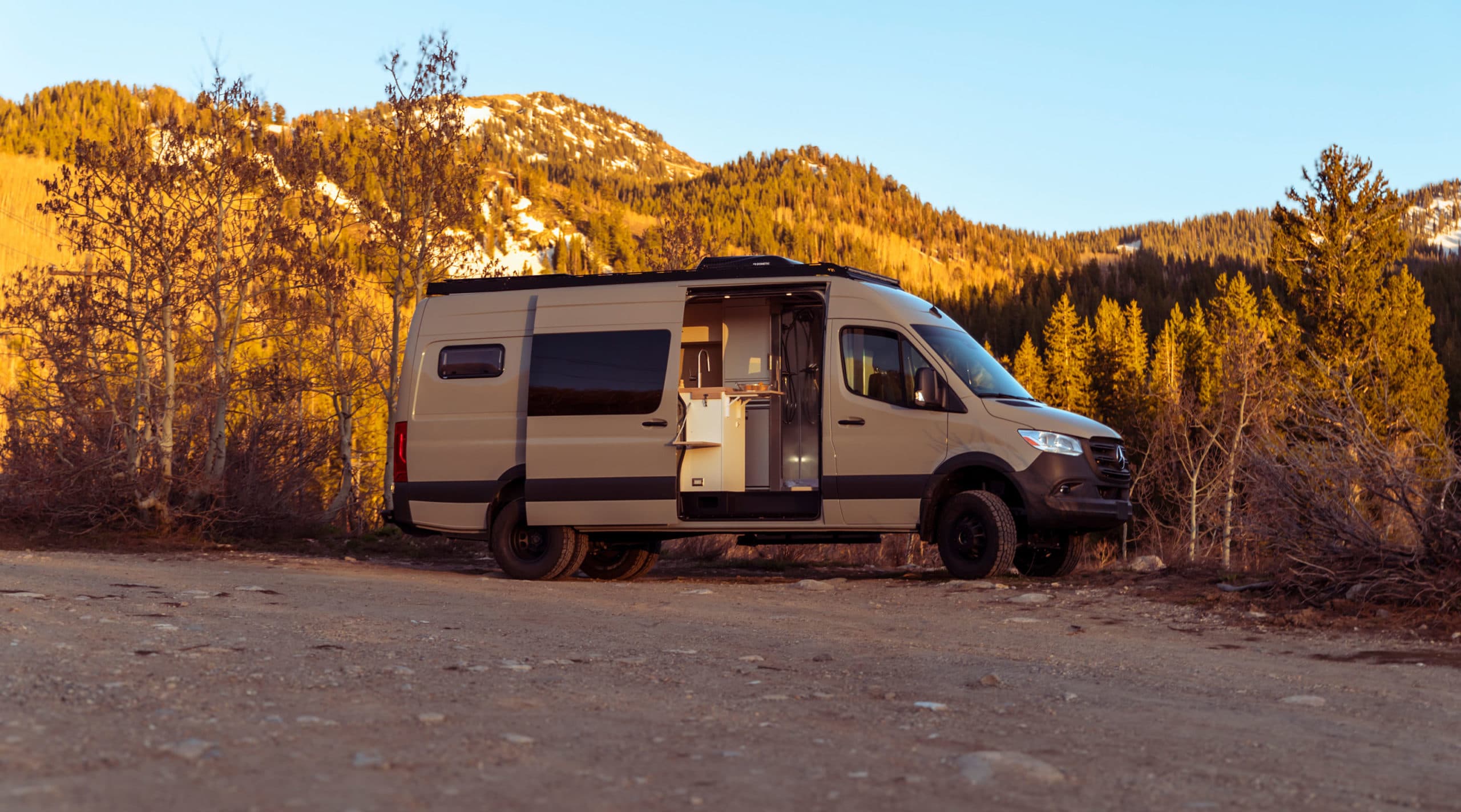 A SAGA-built 4x4 Sprinter 170 in the Utah mountains at sunset, side door open on the galley