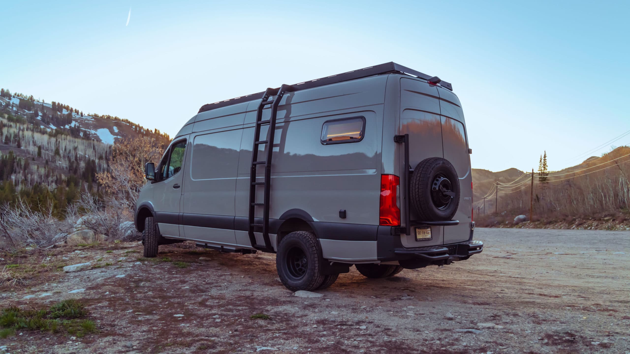 Rear view of 4x4 Sprinter van with roof rack, side ladder, spare tire mount, and all-terrain tires 4x4 Saga Sprinter Van 170