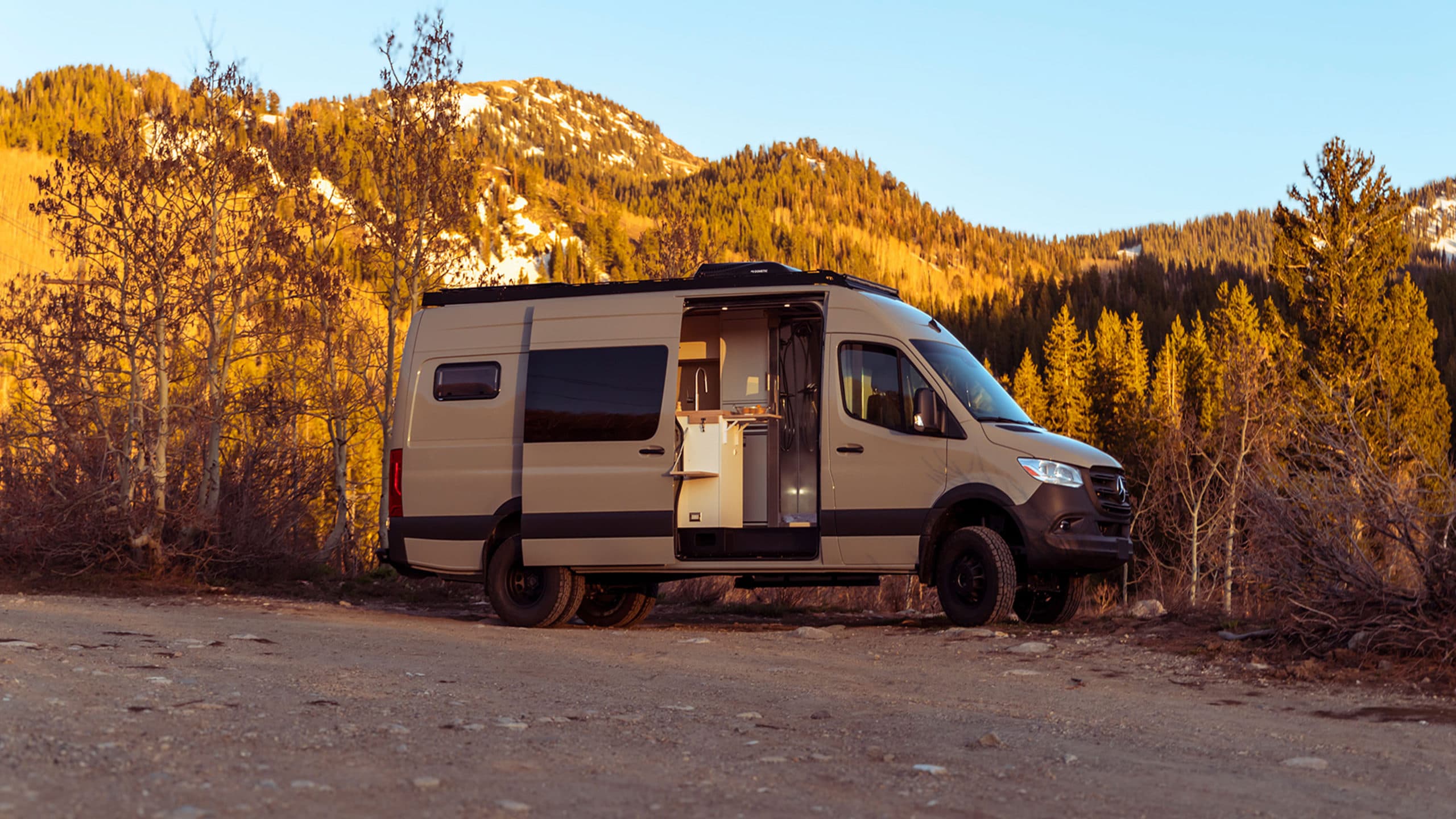 Side view of 4x4 Sprinter van with roof rack, off-road tires, and open sliding door revealing interior kitchen setup 4x4 Saga Sprinter Van 170