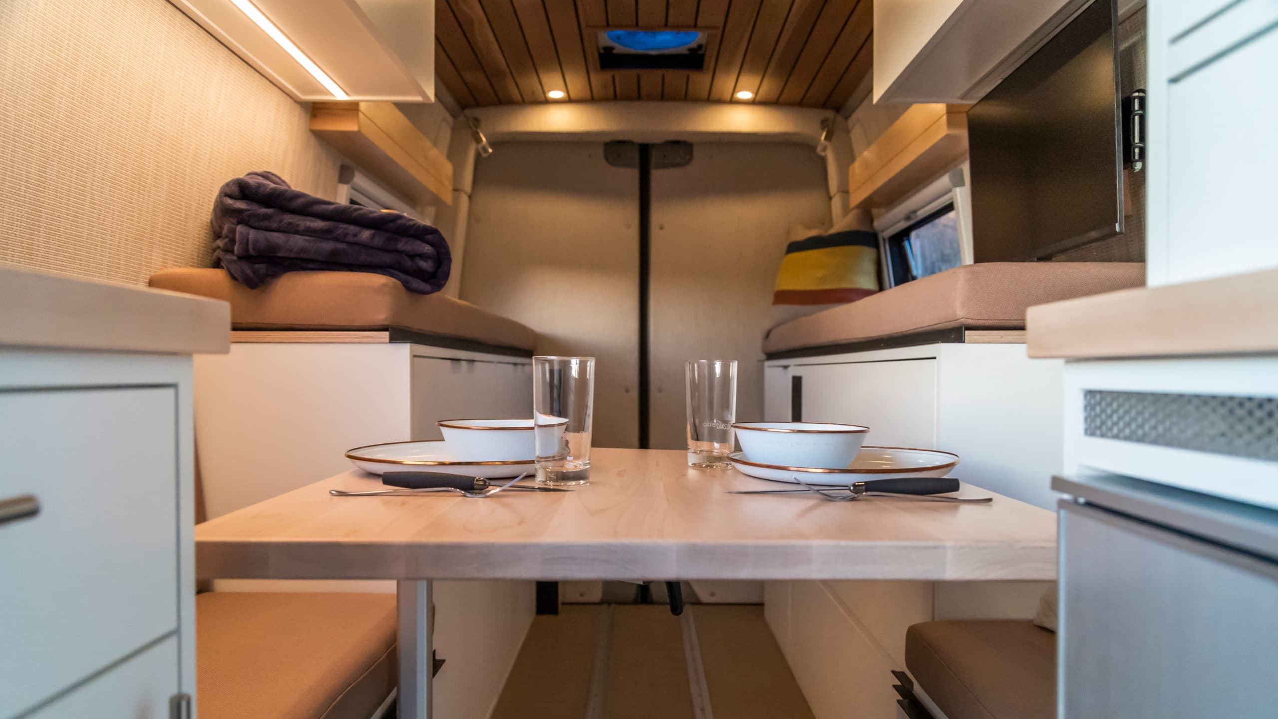 Fold-out dining table with place settings between dual bench seating and overhead storage in 4x4 Saga Sprinter Van 170
