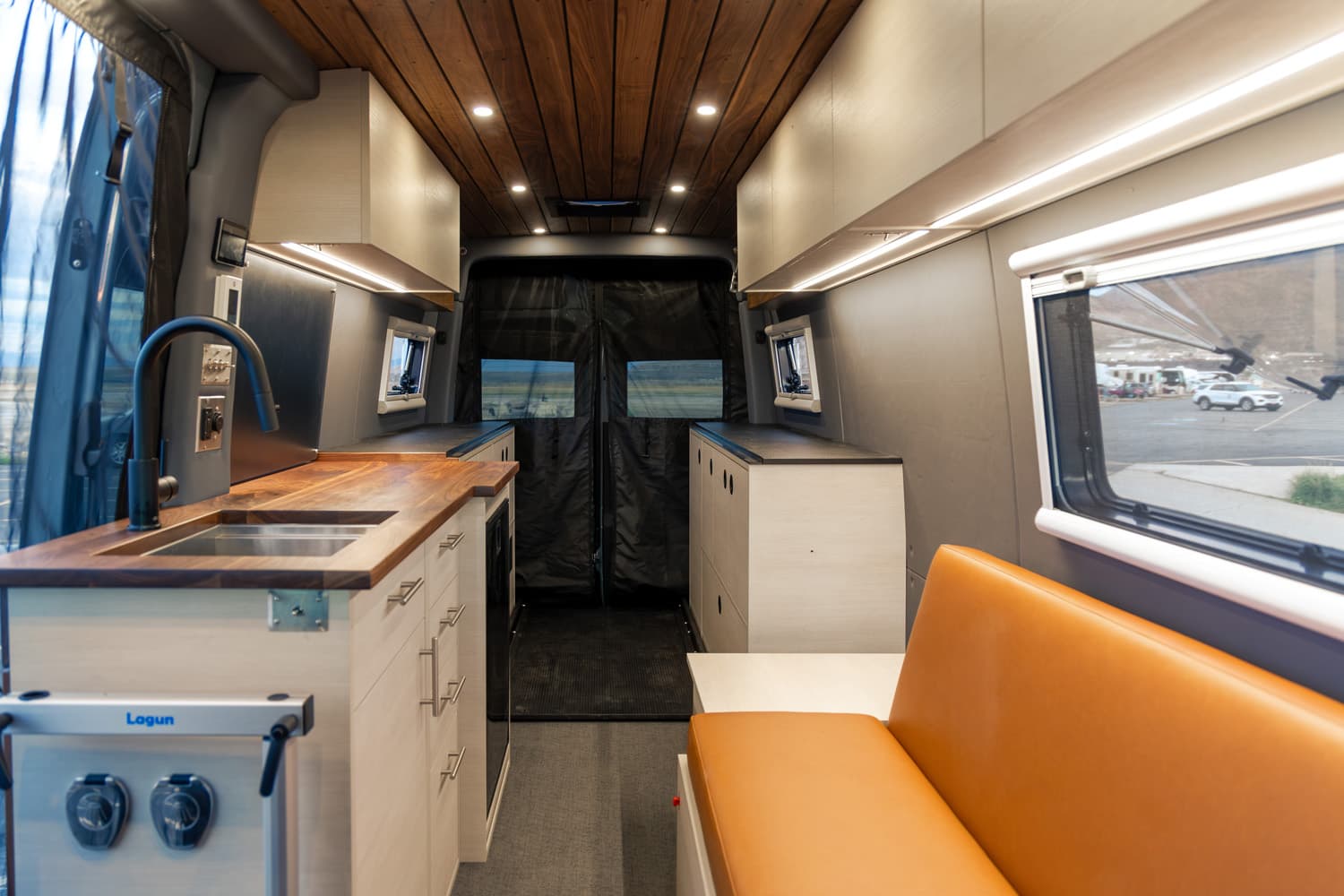 Butcher block countertop with integrated sink, upper storage, leather bench seat, and wood ceiling in 2022 Sprinter 170