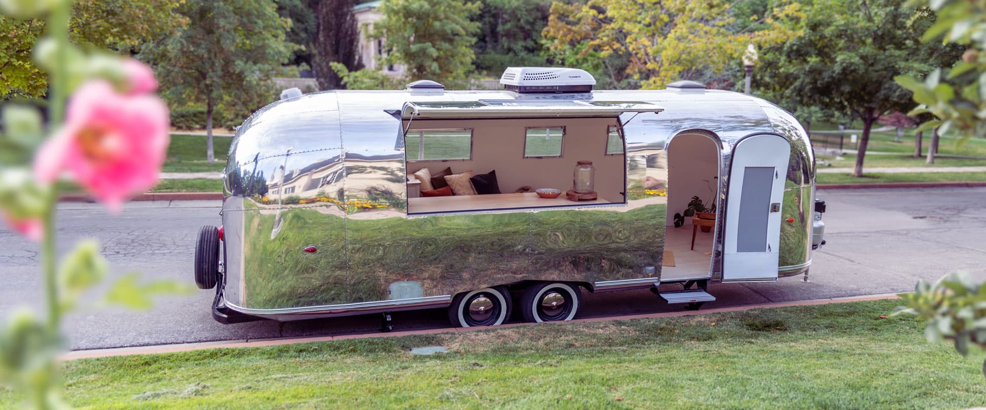 1959 Airstream Tradewind trailer with polished siding parked in a lush green neighborhood